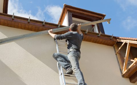 Entretien et réparation de la maison . à l'aide d'une échelle , l'ouvrier controle l'étanchéité de sa toiture et remplace les goutiières